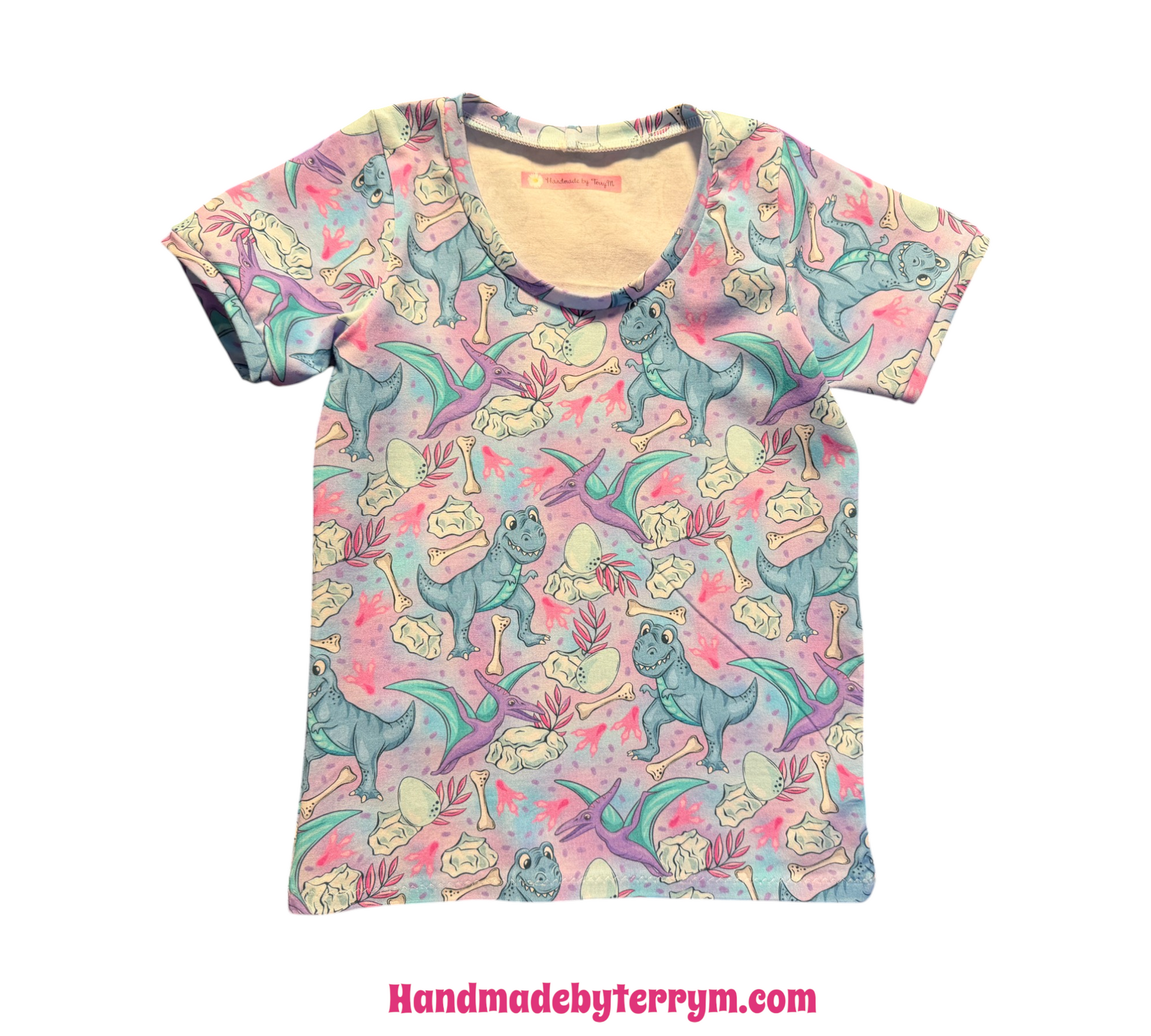A short-sleeve crewneck t-shirt featuring a colorful cartoon dinosaur print on a light pink background, displayed flat against a white background.