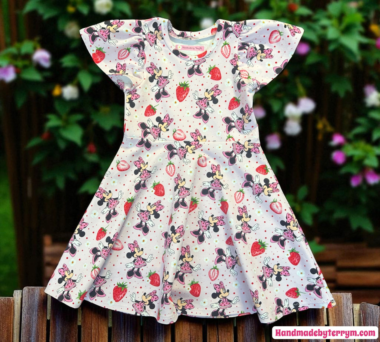 Children's dress with minnie mouse and strawberry pattern on a wooden surface with a garden background