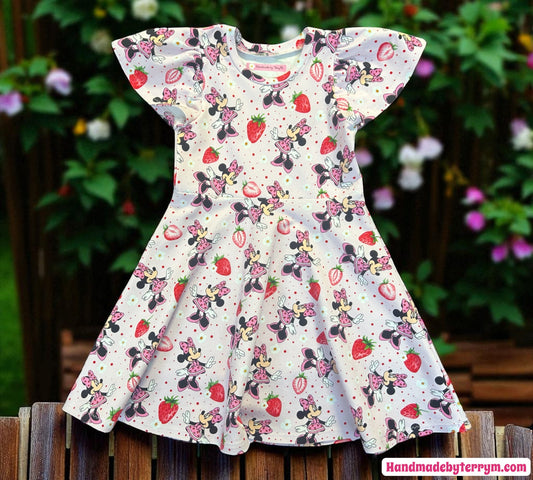 Children's dress with minnie mouse and strawberry pattern on a wooden surface with a garden background